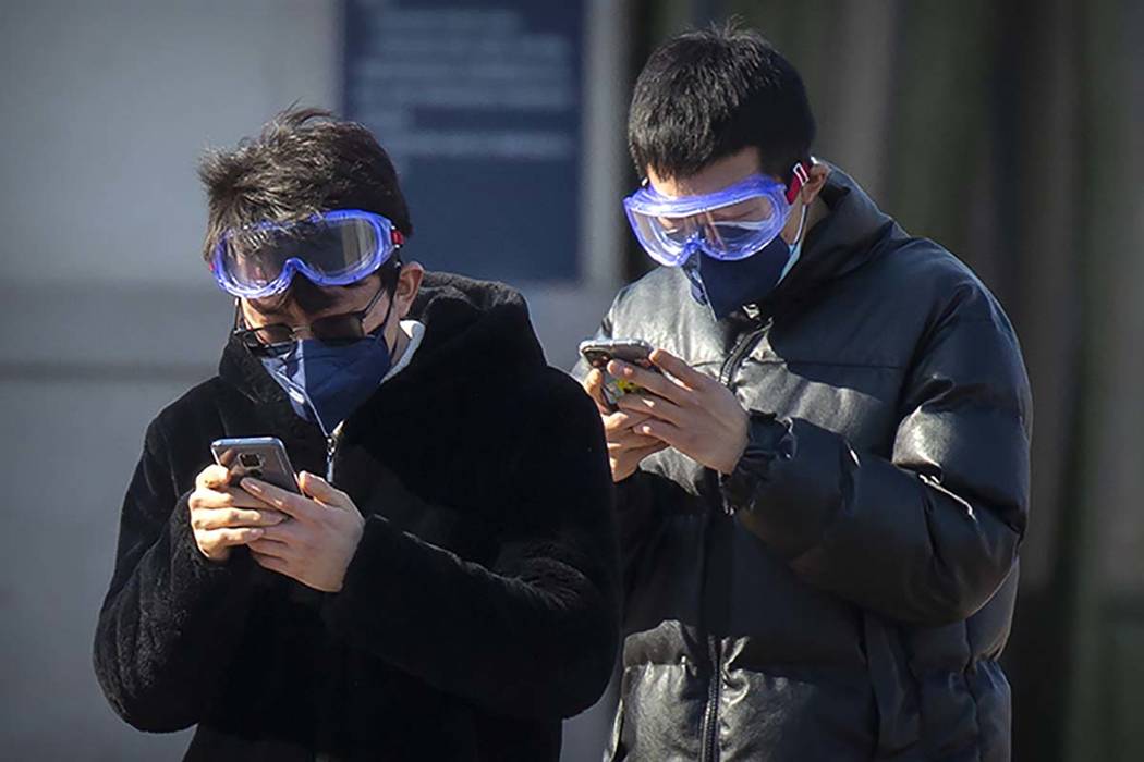 Travelers wear face masks and goggles as they use their smartphones outside the Beijing Railway ...
