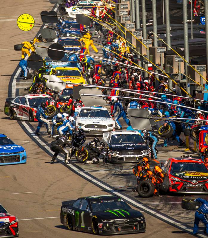 Crews scramble about during the first pit in the Pennzoil 400 presented by Jiffy Lube, a NASCAR ...