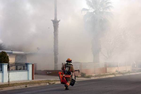 Heavy smoke is seen as a Las Vegas firefighter prepares to battle a house fire at 2417 Howard D ...
