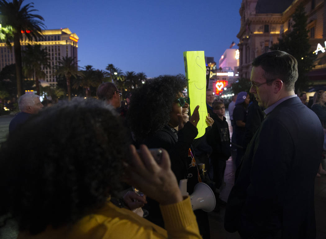 Protesters hold signs on the Strip outside Paris before the start of the Nevada Democratic pres ...