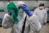 A workers wearing protective gears adjusts her glasses while she prepares to spray disinfectant ...