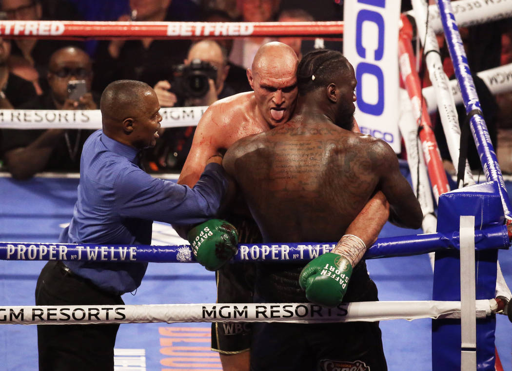 Tyson Fury, left, sticks his tongue out while leaning on Deontay Wilder in the fifth round duri ...