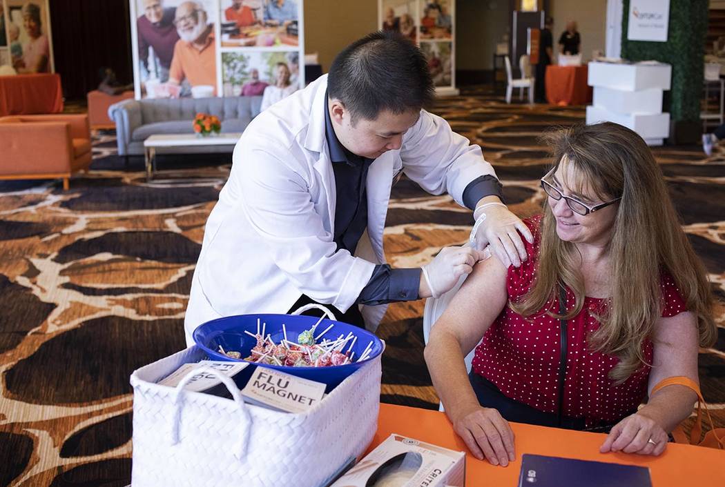 Vons Pharmacy intern Kevin Chang cleans Brenda Julian's upper arm in preparation for a flu shot ...