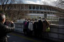 Tourists wear masks as they pause for photos with the New National Stadium, a venue for the ope ...