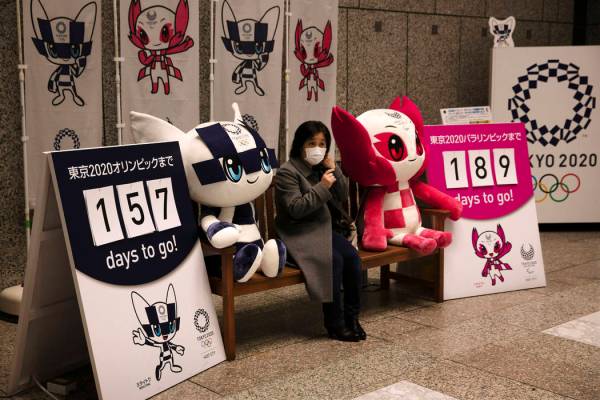 A woman removes her mask before taking pictures with the mascots of the Tokyo 2020 Olympics and ...