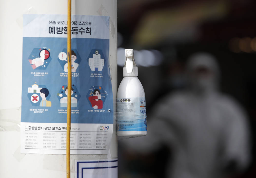 A bottle of hand sanitizers hangs on a pole on a street for visitors next to notices about prec ...