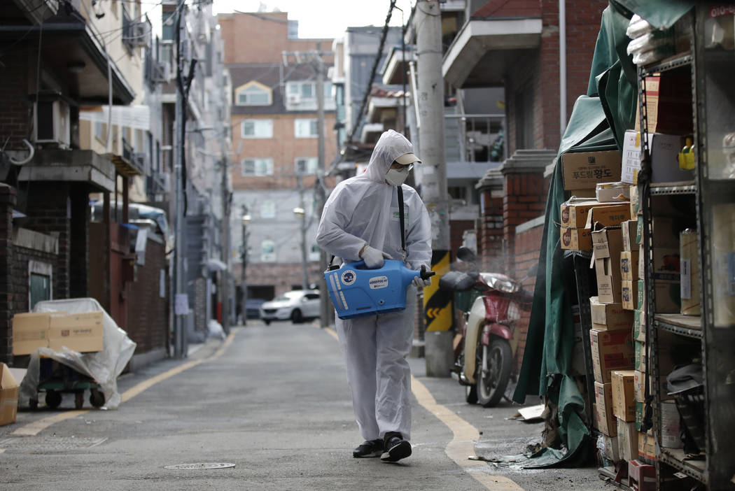 A worker wearing a protective suit sprays disinfectant as a precaution against new virus at a m ...