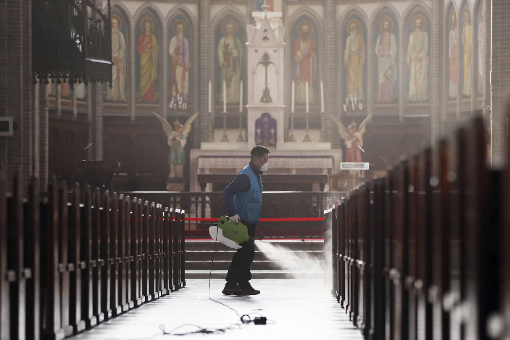 A worker wearing a face mask sprays disinfectant as a precaution against the new coronavirus at ...