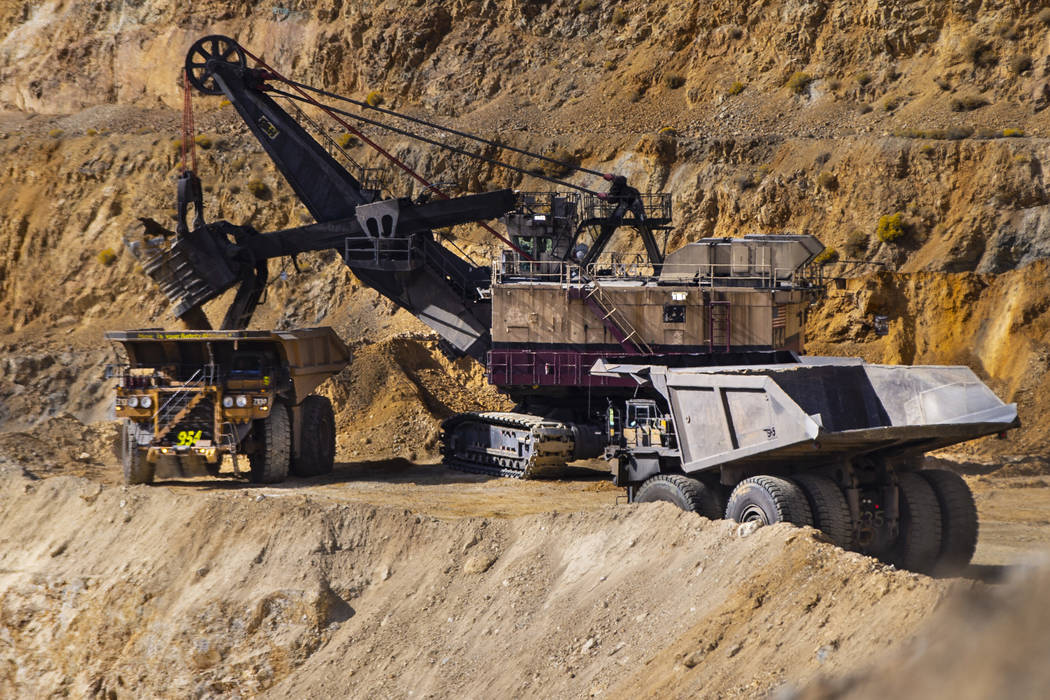 Haul trucks that can carry over 300 tons of material line up by a large excavator at Nevada Gol ...