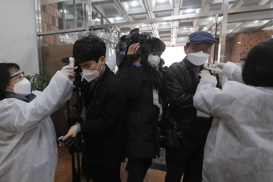 People check the temperature of journalists wearing face masks as they enter the Yoido Full Gos ...