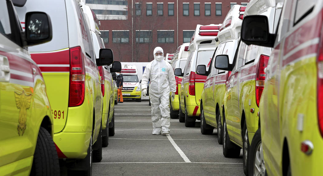 A health worker wearing a protective suit walks between the ambulances to transport patients in ...