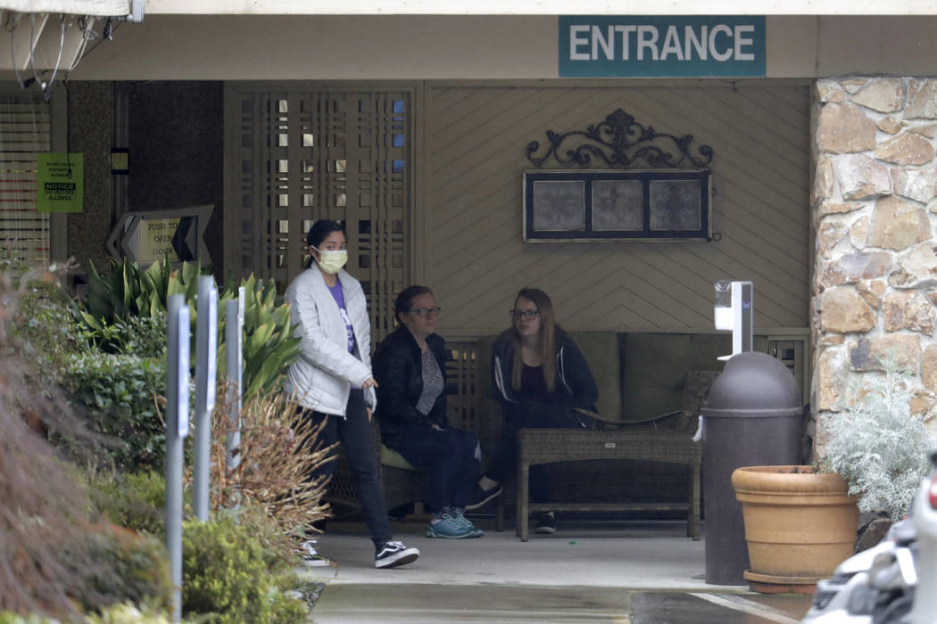 A person wearing a mask walks past a sign banning visitors at the Life Care Center in Kirkland, ...