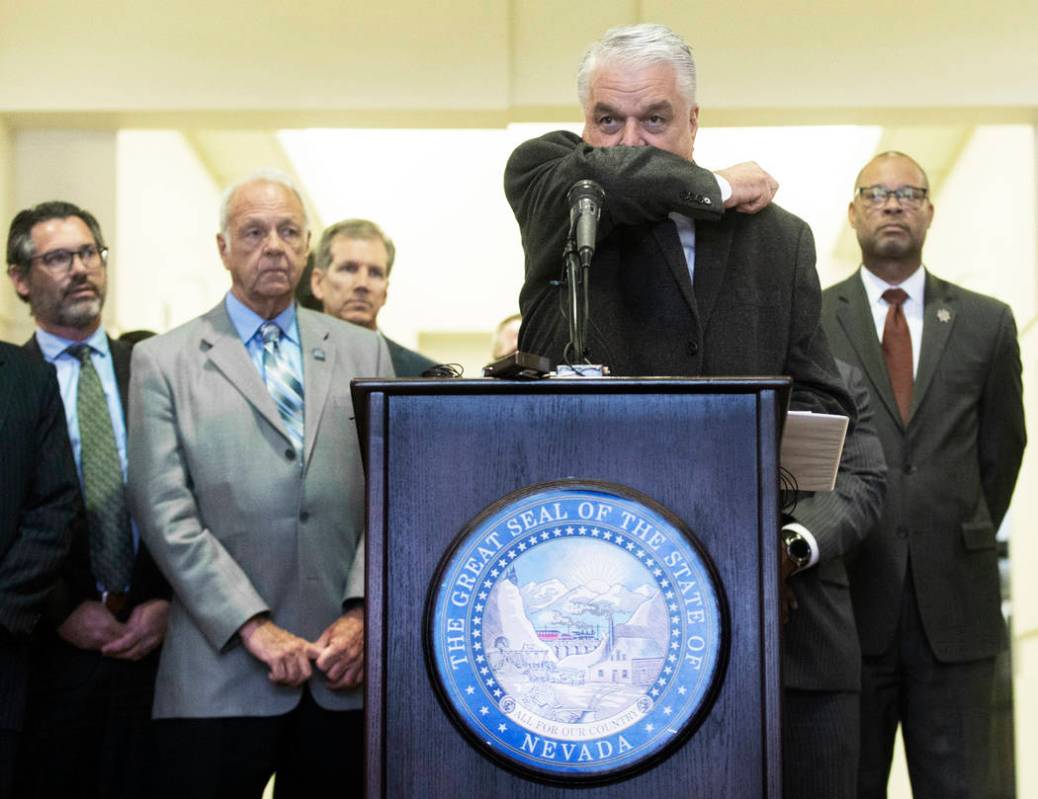 Gov. Steve Sisolak demonstrates the best way to cough without spreading disease during a press ...
