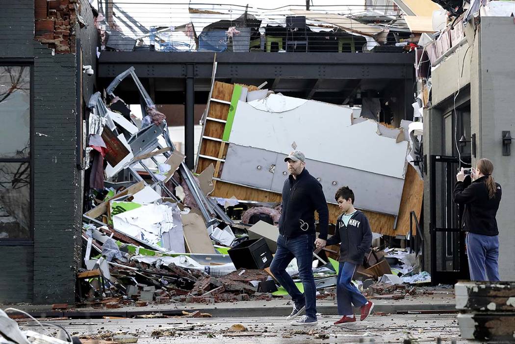 People walk past buildings damaged by storms Tuesday, March 3, 2020, in Nashville, Tenn. Tornad ...