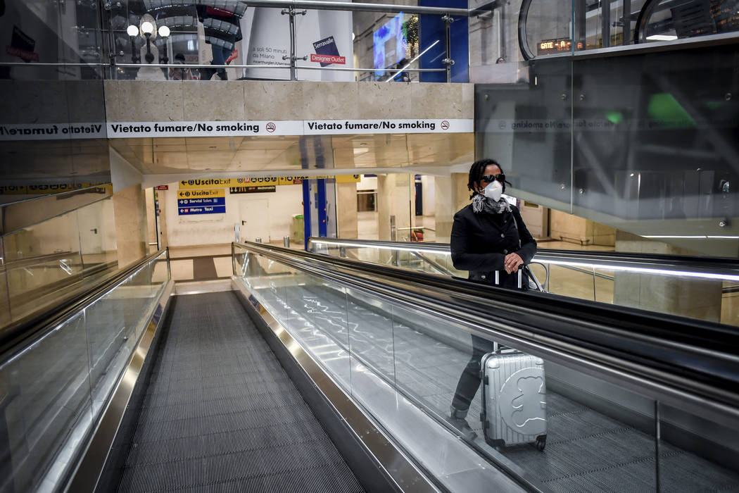 A woman wears a mask as she stands on an escalator inside Central train station, in Milan, Ital ...