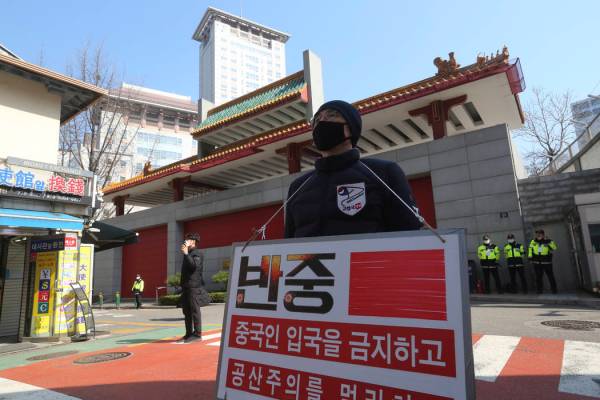 A man wearing a face mask stands calling for a ban on Chinese people entering South Korea near ...