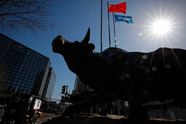A delivery worker ride his cart passes by the investment icon bull statue on display outside a ...