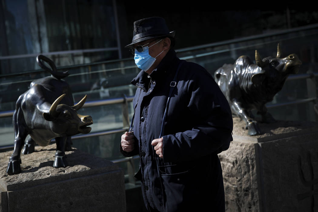 A man wearing a protective face mask walks by statues of bulls on display outside a bank in Bei ...