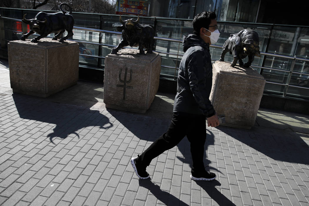 A man wearing a protective face mask walks by statues of bulls on display outside a bank in Bei ...