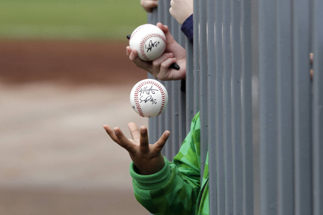 A child tosses an already-autographed baseball while awaiting another signature from a passing ...