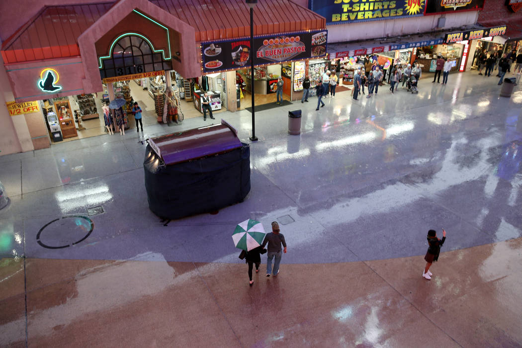 People walk in a light rain at the Fremont Street Experience in downtown Las Vegas Thursday, Ma ...