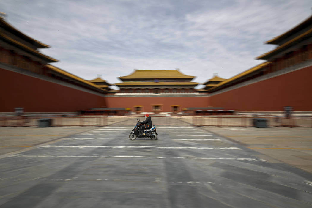 A man rides on an electric-powered scooter passes by the closed entrance gates to the Forbidden ...