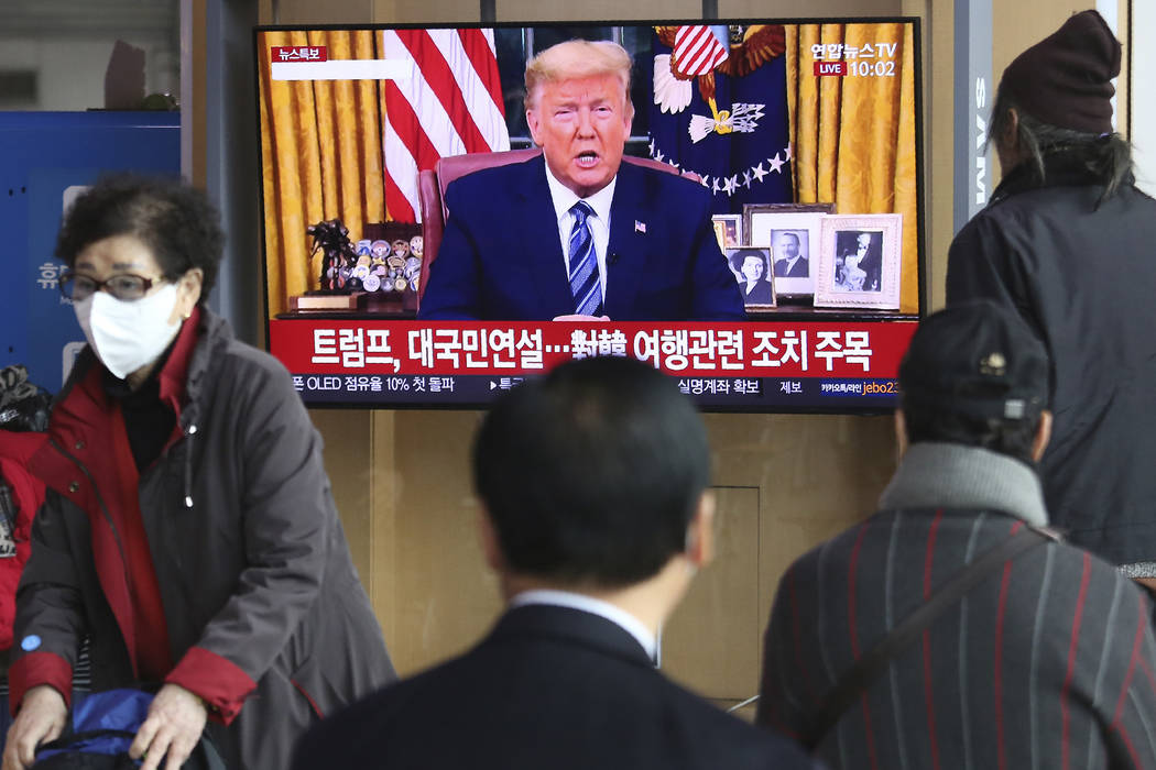 People watch a TV screen showing a live broadcast of U.S. President Donald Trump's speech at th ...