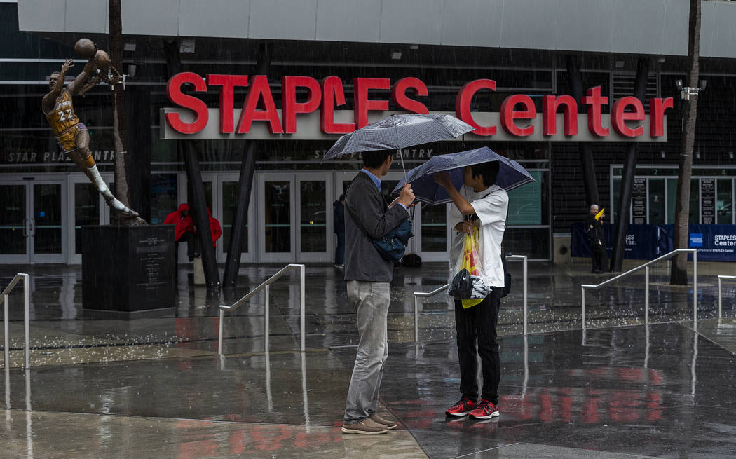 Tourist stand under umbrellas in rain outside Staples Center, home to hockey's Los Angeles King ...