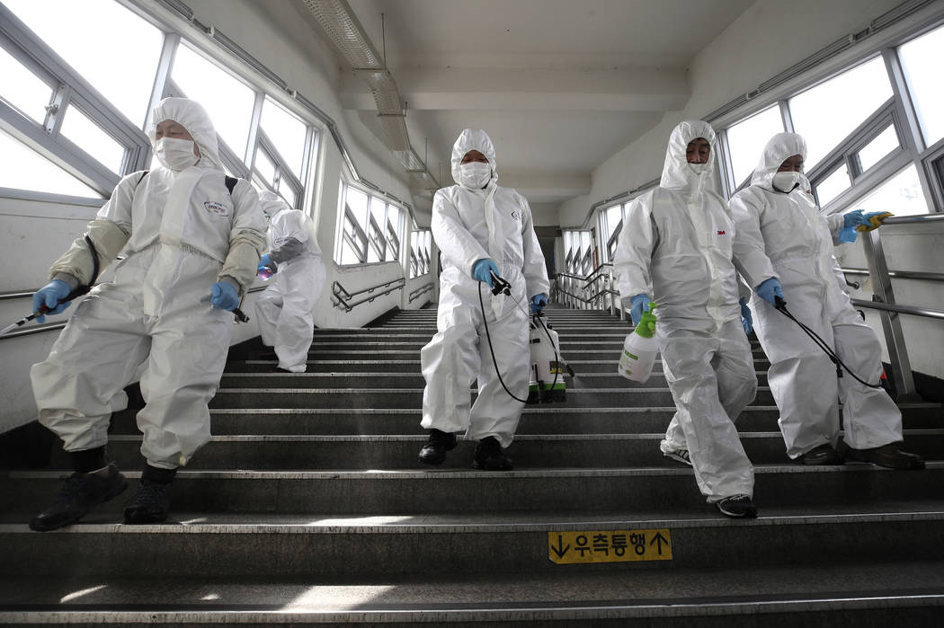 Workers wearing protective suits spray disinfectant as a precaution against the new coronavirus ...
