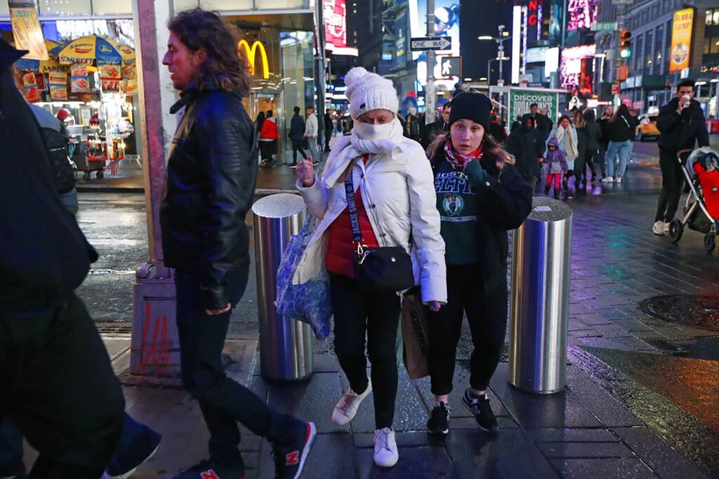 Tourists, including one using a scarf to protect her face against coronavirus in spite of relat ...