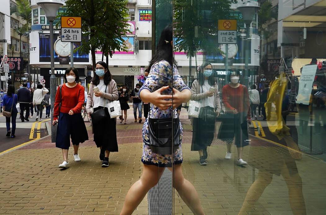 People wearing face masks walk at a street in Hong Kong Friday, March. 13, 2020. For most, the ...