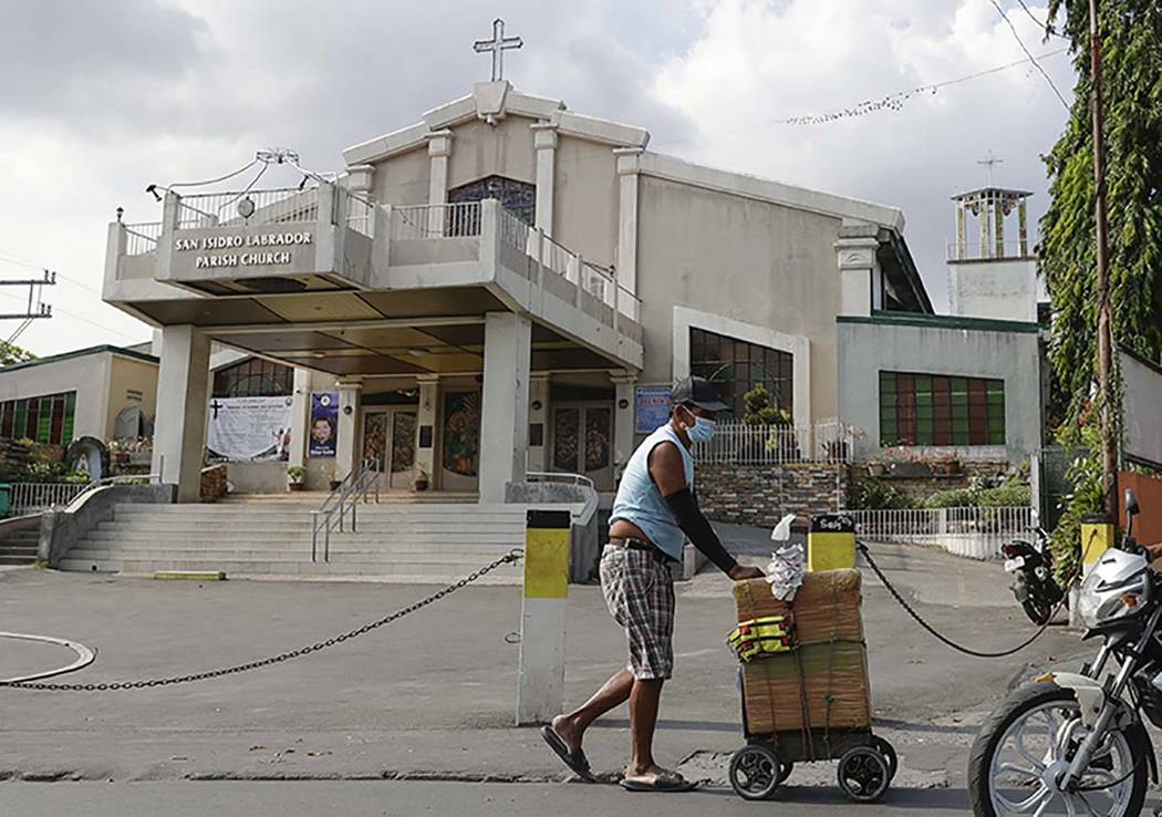 A vendor wearing a protective mask walks past a church in suburban Quezon city, in Manila, Phil ...