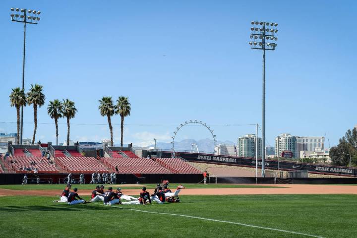 UNLV sits on the field while warming up before a game against UNR during an NCAA baseball game ...