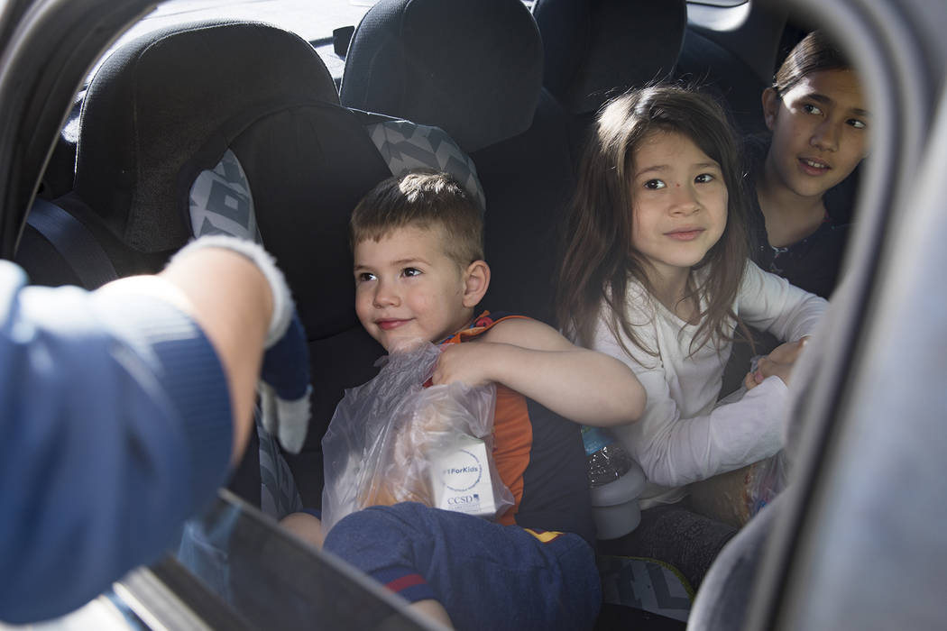 A Clark County School District employee hands packaged food to siblings Michael Randal, 3, left ...