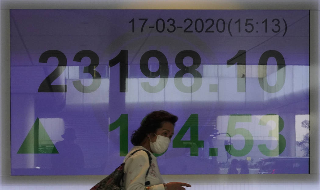 A woman wearing face mask walks past a bank electronic board showing the Hong Kong share index ...