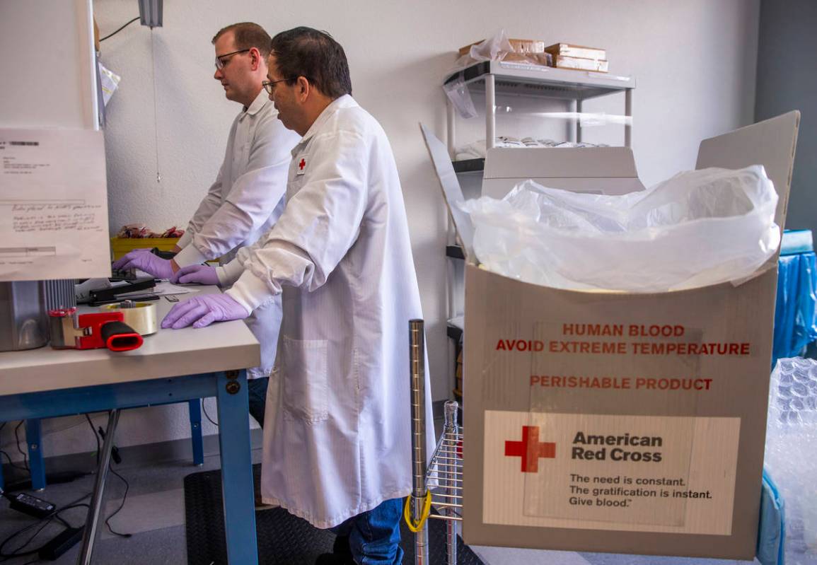 Red Cross team members Rudy Delos-Santos, left, and Kyle Best log in new blood donations and pr ...