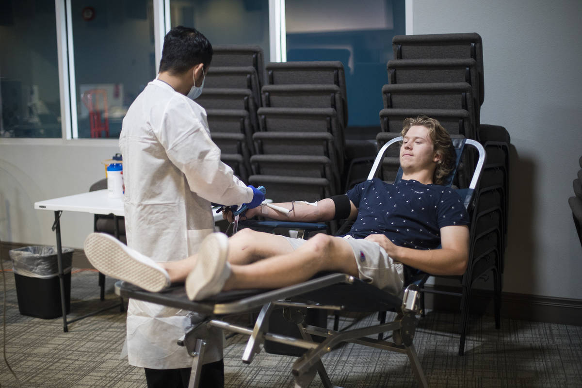 Ernesto Perez, a phlebotomist tech and supervisor, helps William Buening, 17, as he gives blood ...