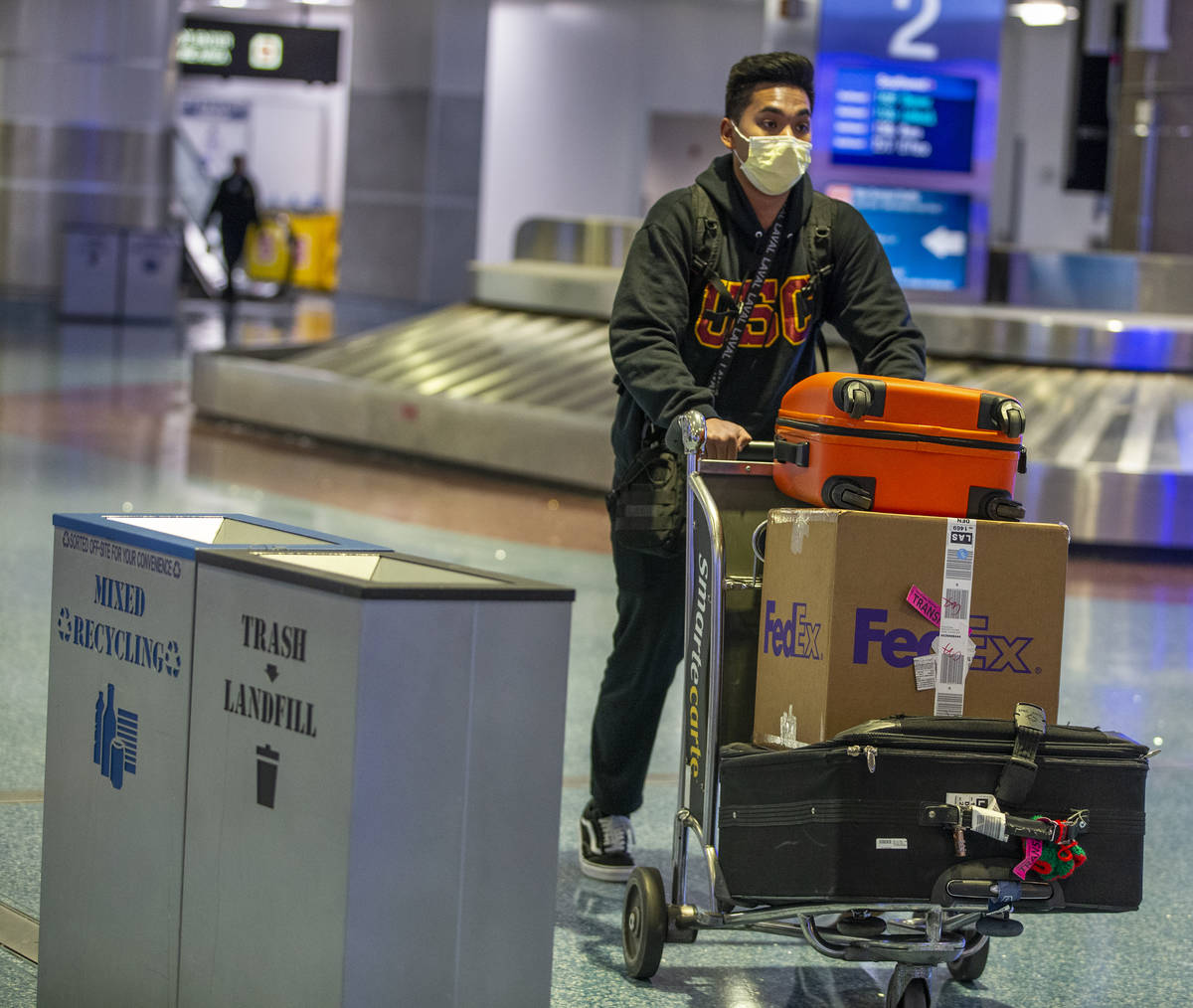A masked passenger wheels his luggage from the baggage area in Terminal 1 at McCarran Internati ...