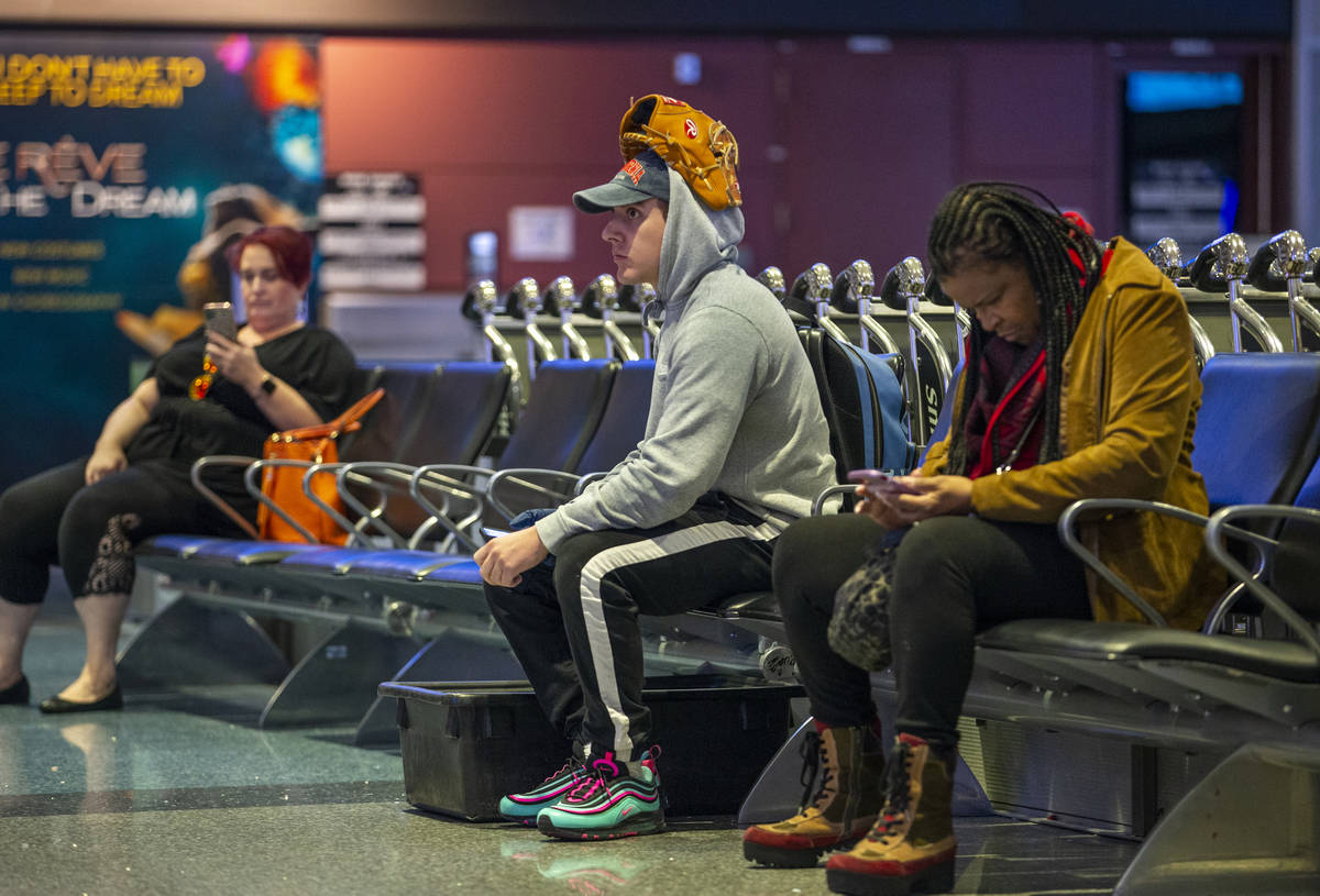Passenger Montana Gomez wears his baseball glove on his head while waiting in the baggage area ...