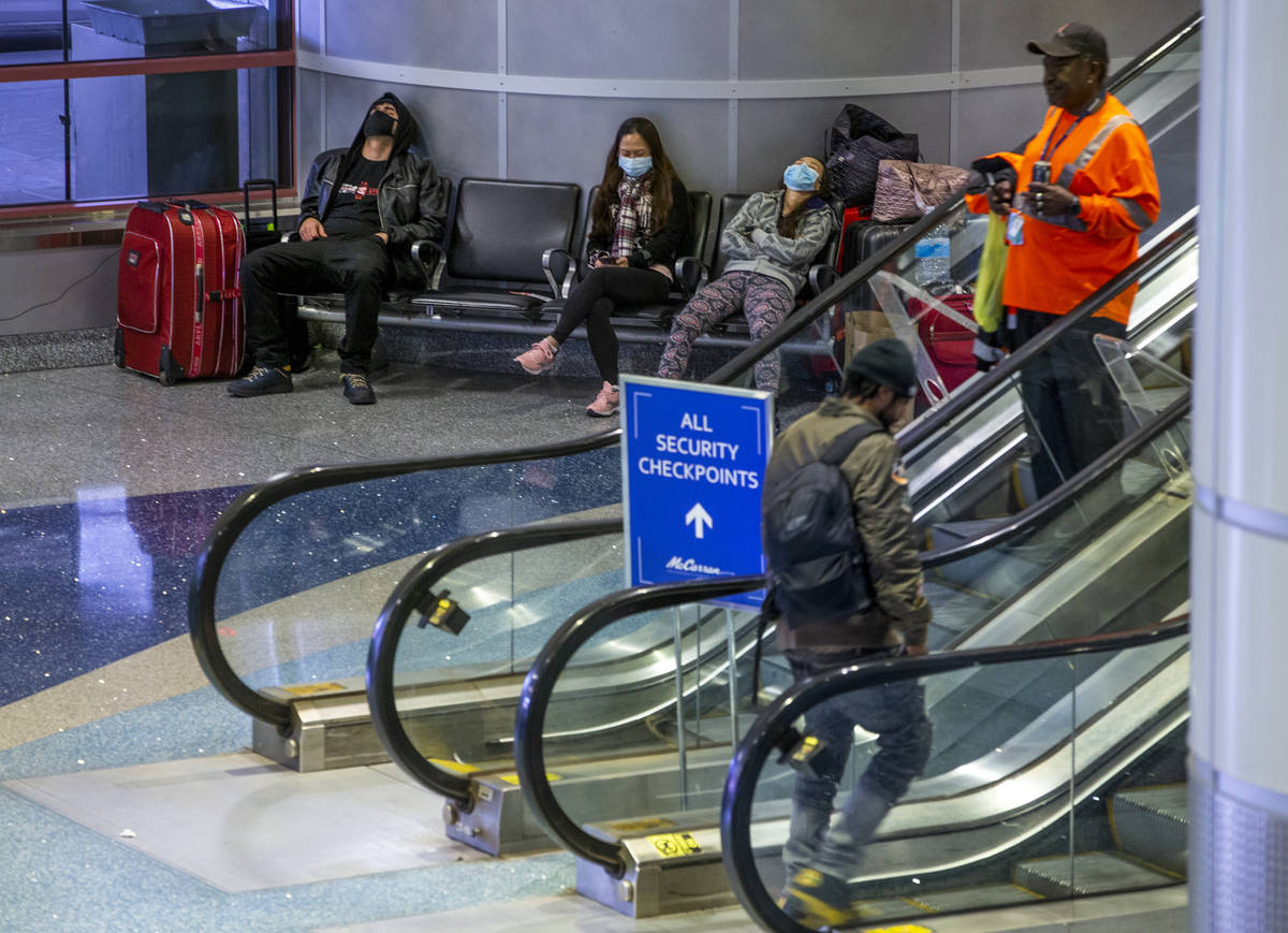 Passengers in masks kill some time awaiting their flights with others in the ticketing area of ...