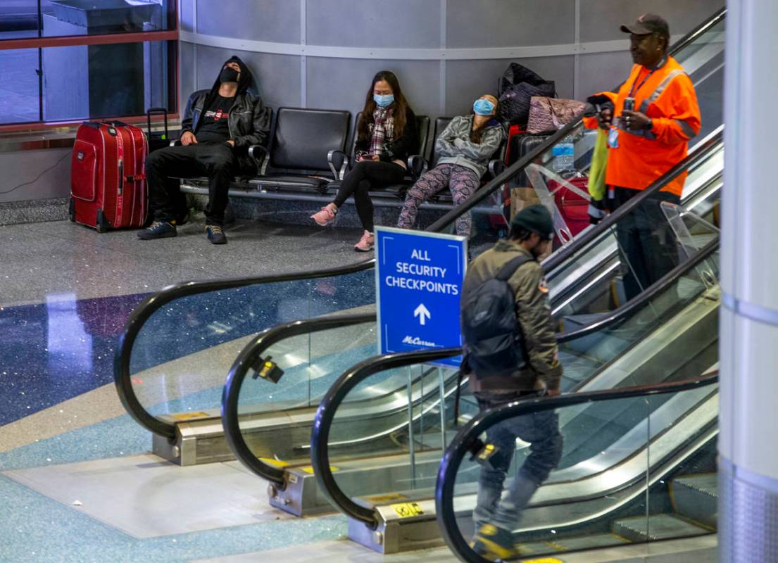 Passengers in masks kill some time awaiting their flights with others in the ticketing area of ...