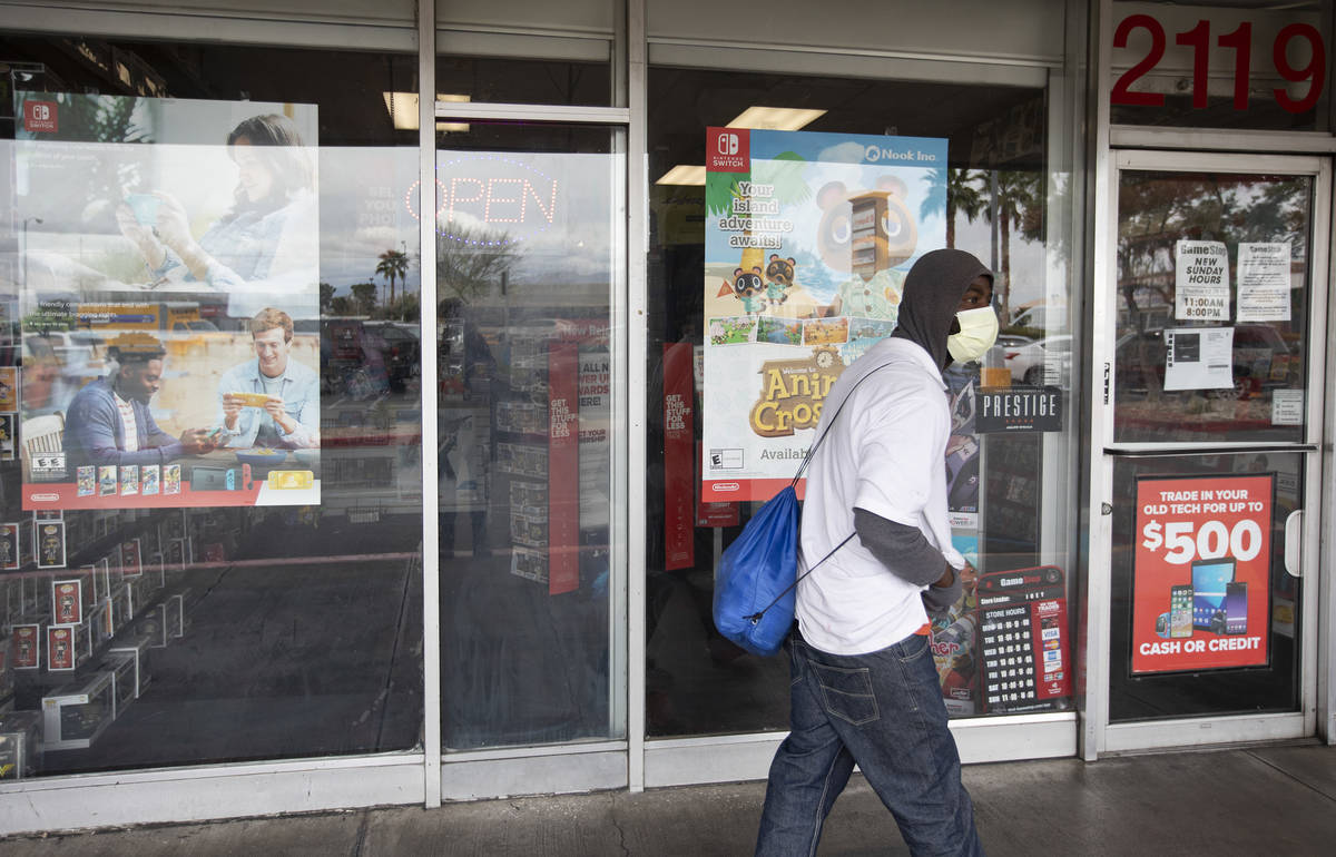A masked person walks past the GameStop store at 2119 East Lake Mead Boulevard, which remains o ...