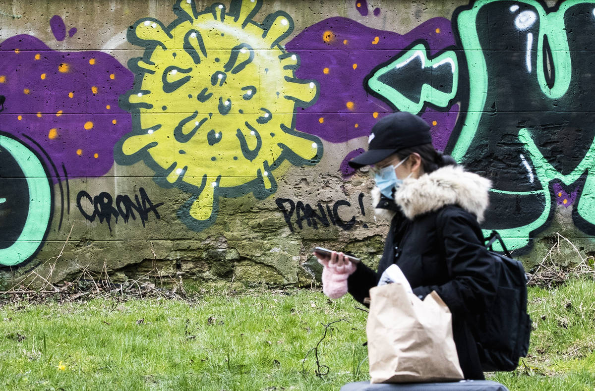 A woman walks by coronavirus graffiti, in Edinburgh, Scotland, Saturday March 21, 2020. For som ...