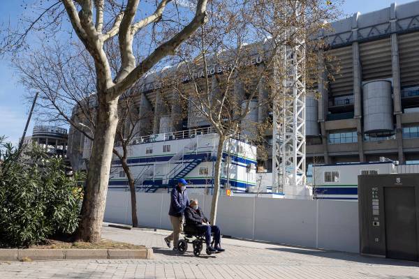 A man is pushed in the wheelchair while wearing protective masks near Real Madrid's Santiago Be ...