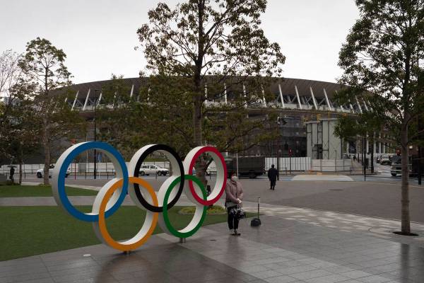 A woman pauses for photos next to the Olympic rings near the New National Stadium in Tokyo, Mon ...