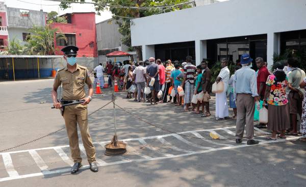 Sri Lankans queue for kerosene as a police officer stands guard during a temporary lift of a c ...
