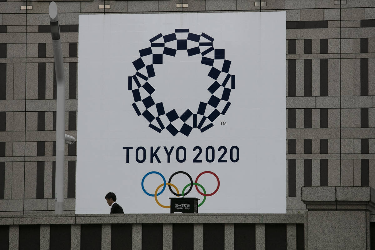 A man walks past a large banner promoting the Tokyo 2020 Olympics in Tokyo, Monday, March 23, 2 ...