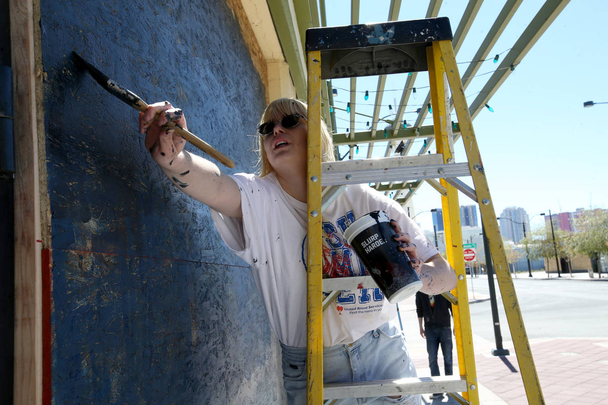 Artist Adelia Hoff paints a mural on the boarded up windows and door of Main Street Mercantile ...