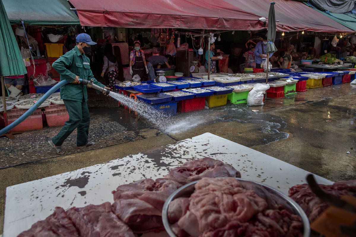 A sanitation worker uses a high-pressure water source to wash a market in Bangkok, Thailand, We ...