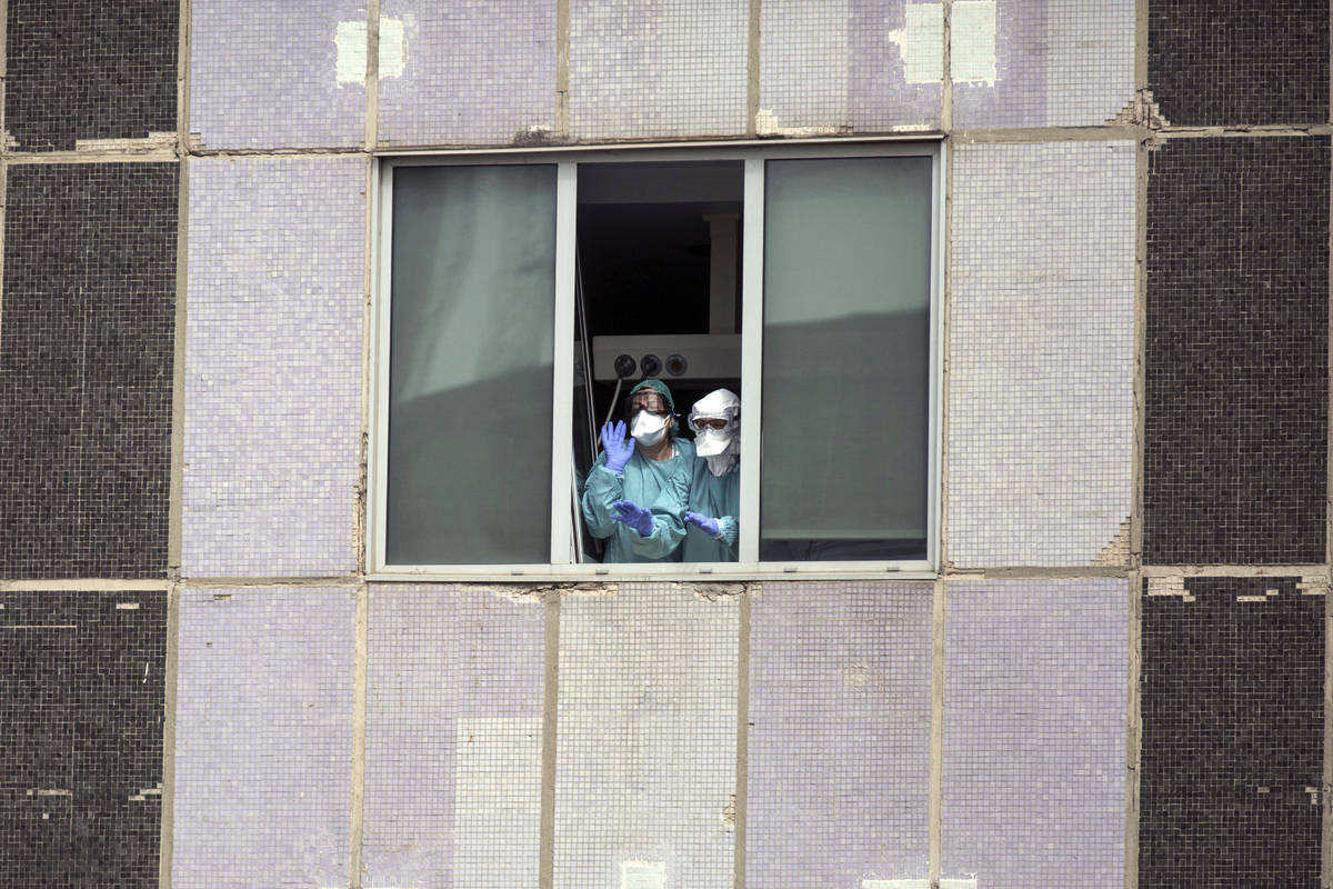 In a Wednesday, March 18, 2020, file photo, medical workers wearing face masks gesture from hos ...